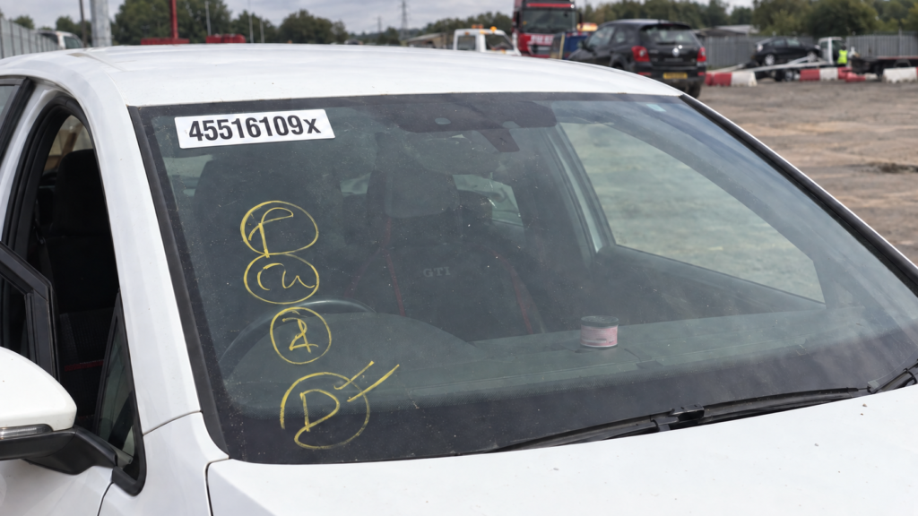 Close-up of a salvage car windscreen with yellow auction yard markings and a white lot-number sticker ending in X