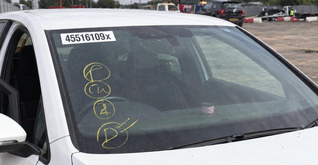 Close-up of a salvage car windscreen with yellow auction yard markings and a white lot-number sticker ending in X