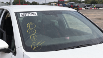 Close-up of a salvage car windscreen with yellow auction yard markings and a white lot-number sticker ending in X
