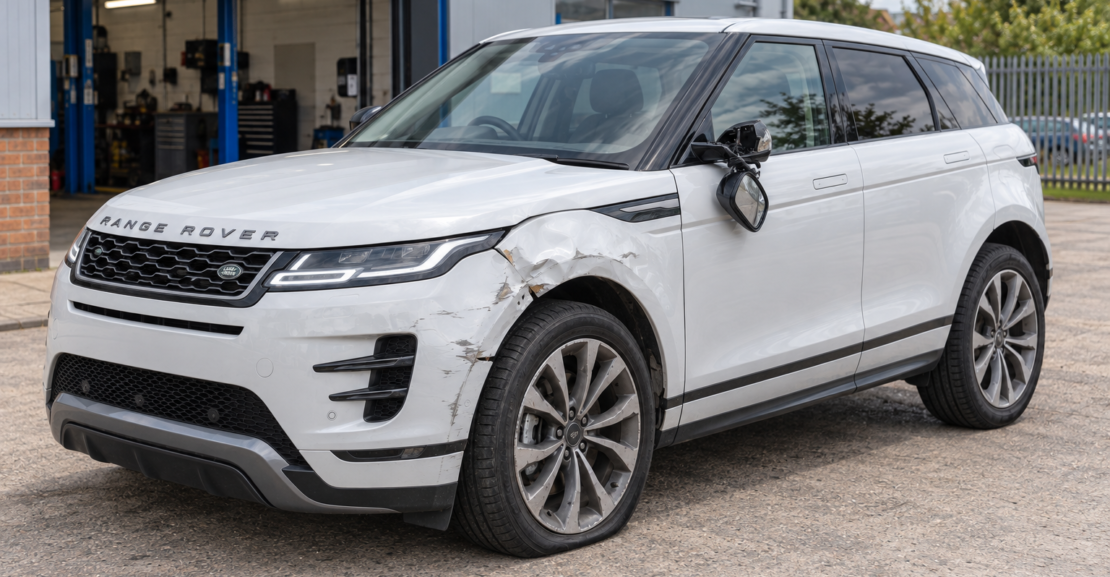 White Range Rover Evoque facing left with a dented front nearside wing, scraped bumper, broken mirror and soft tyre