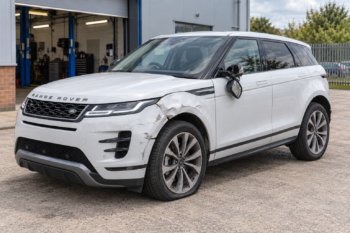White Range Rover Evoque facing left with a dented front nearside wing, scraped bumper, broken mirror and soft tyre